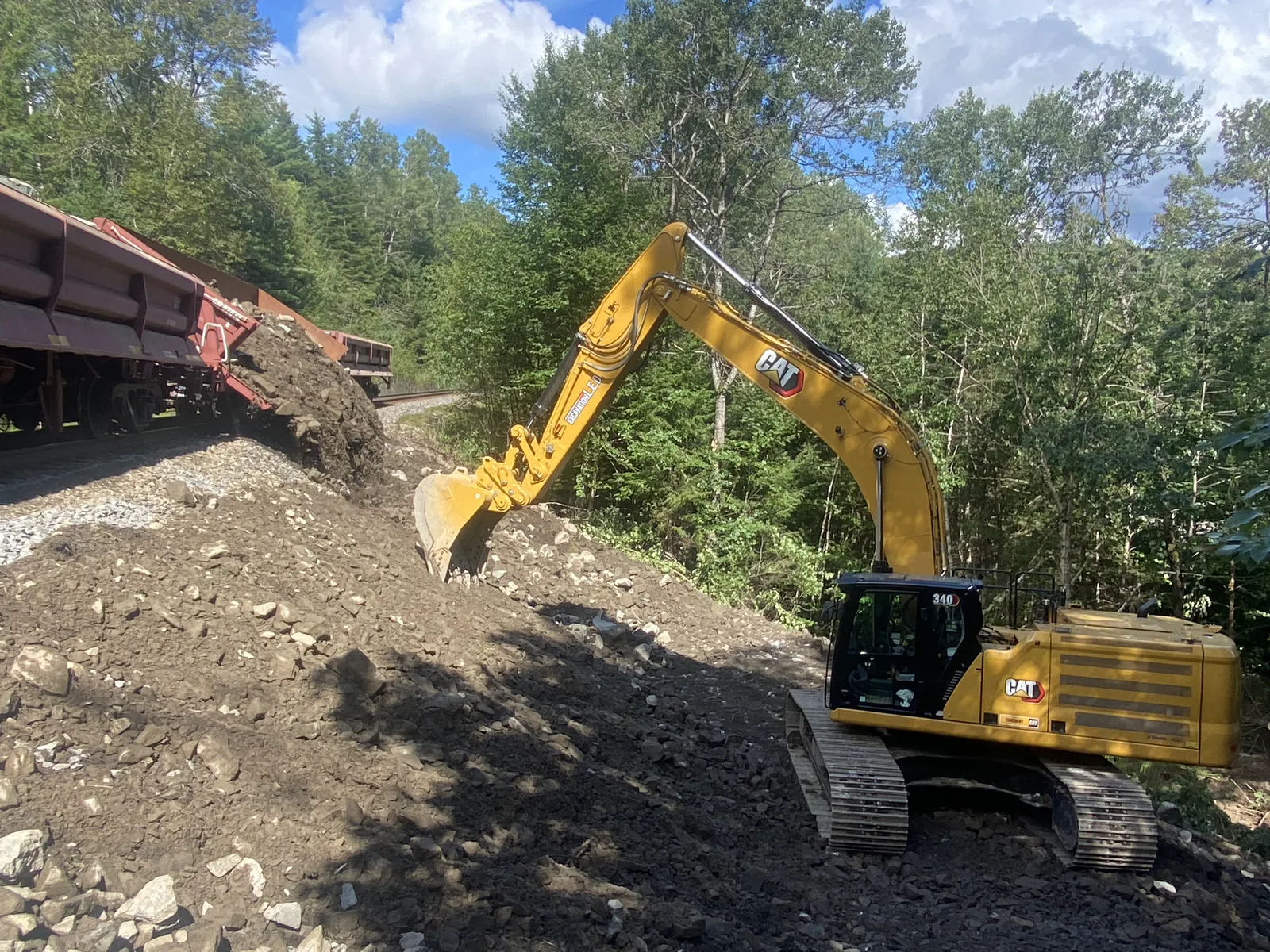 Talus de voie ferrée — Pelle Caterpillar sur le talus d'une voie ferrée, wagons à côté.