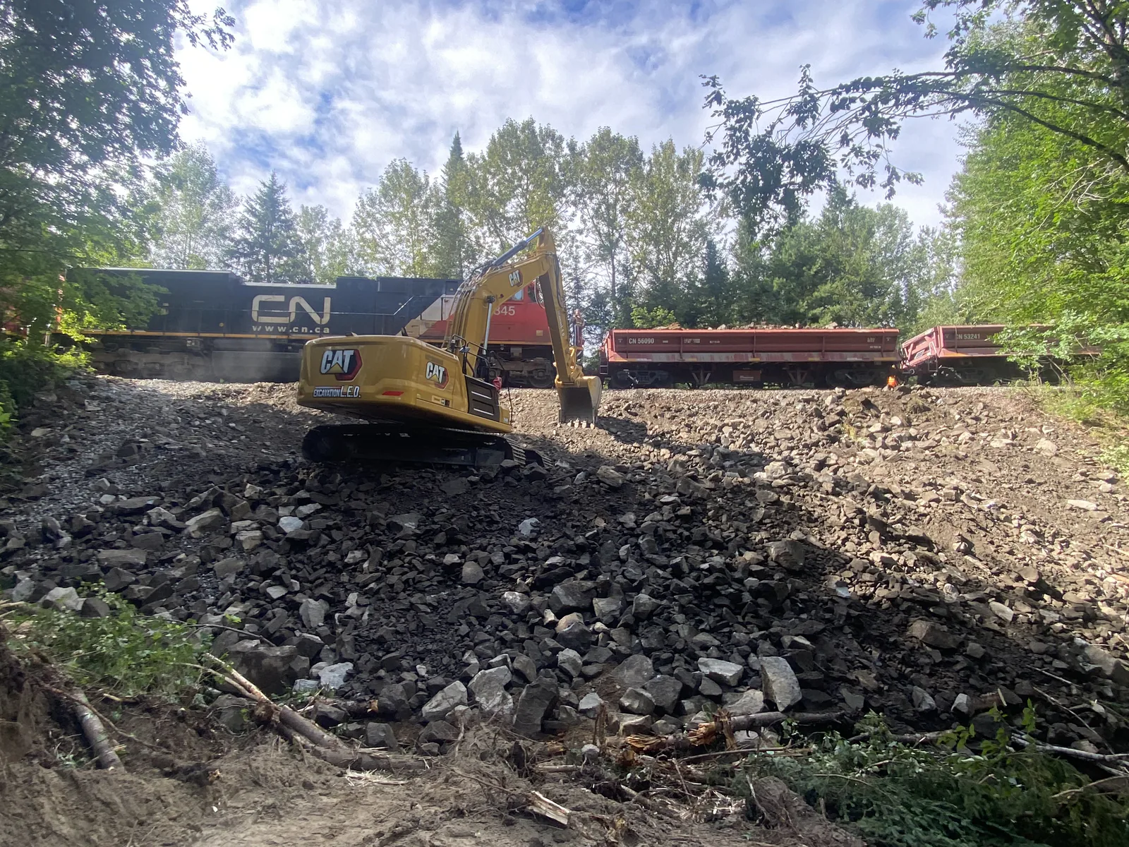 Travaux le long d'une voie ferrée — Pelle Caterpillar sur un remblai de roc, wagons sur la voie ferrée.